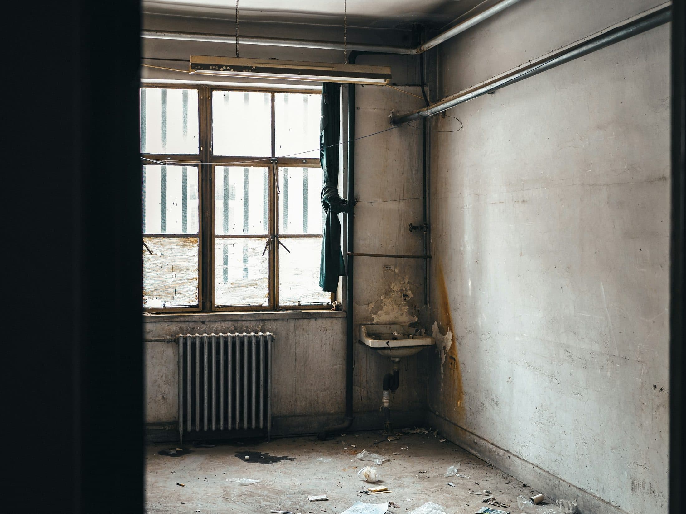 Pièce insalubre : sol souillé, vieux radiateur et lavabo