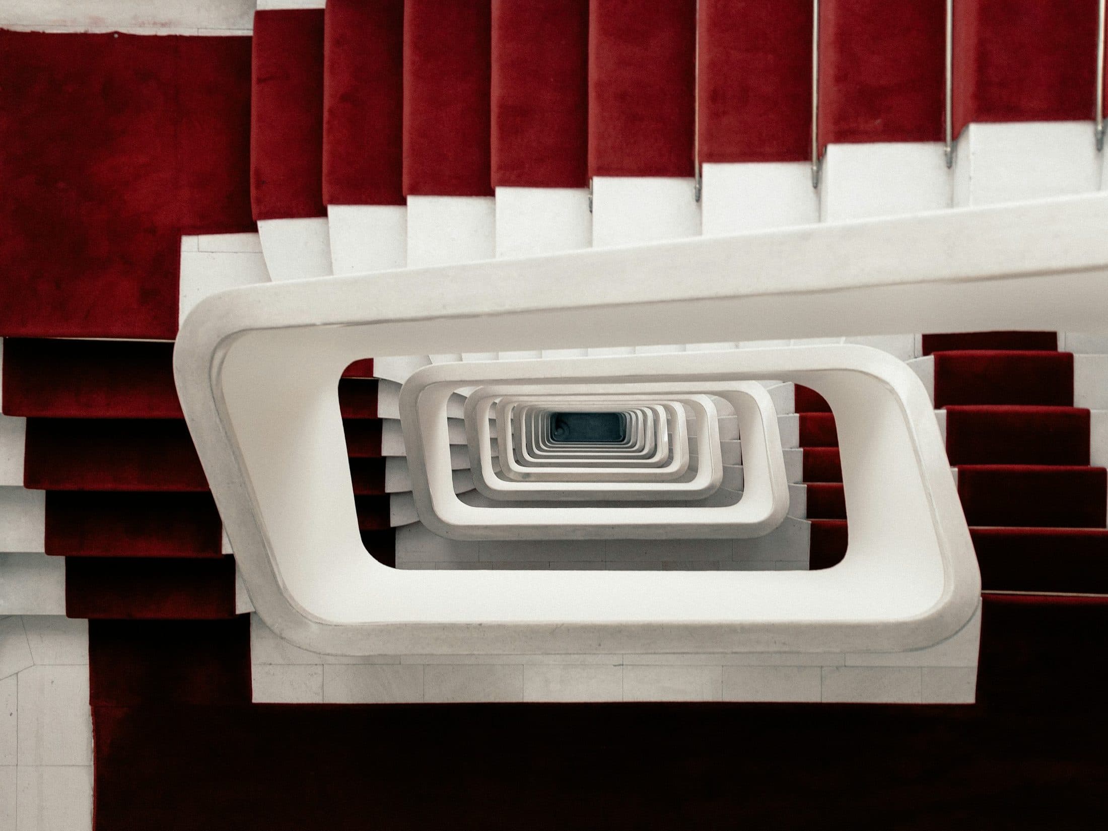 Cage d'escalier vue en plongée, tapis rouge courant sur les marches